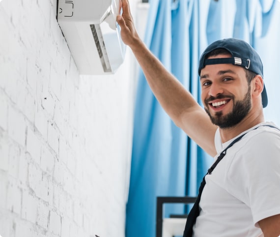 HVAC technician smiling while adjusting a wall-mounted air conditioning unit, showcasing quality heating and cooling services at Dale-Air in San Diego.