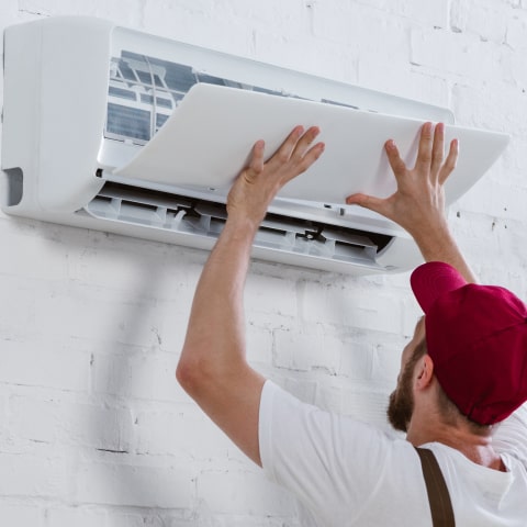 HVAC technician performing maintenance on a wall-mounted air conditioning unit in a residential setting, emphasizing quality service and expertise.