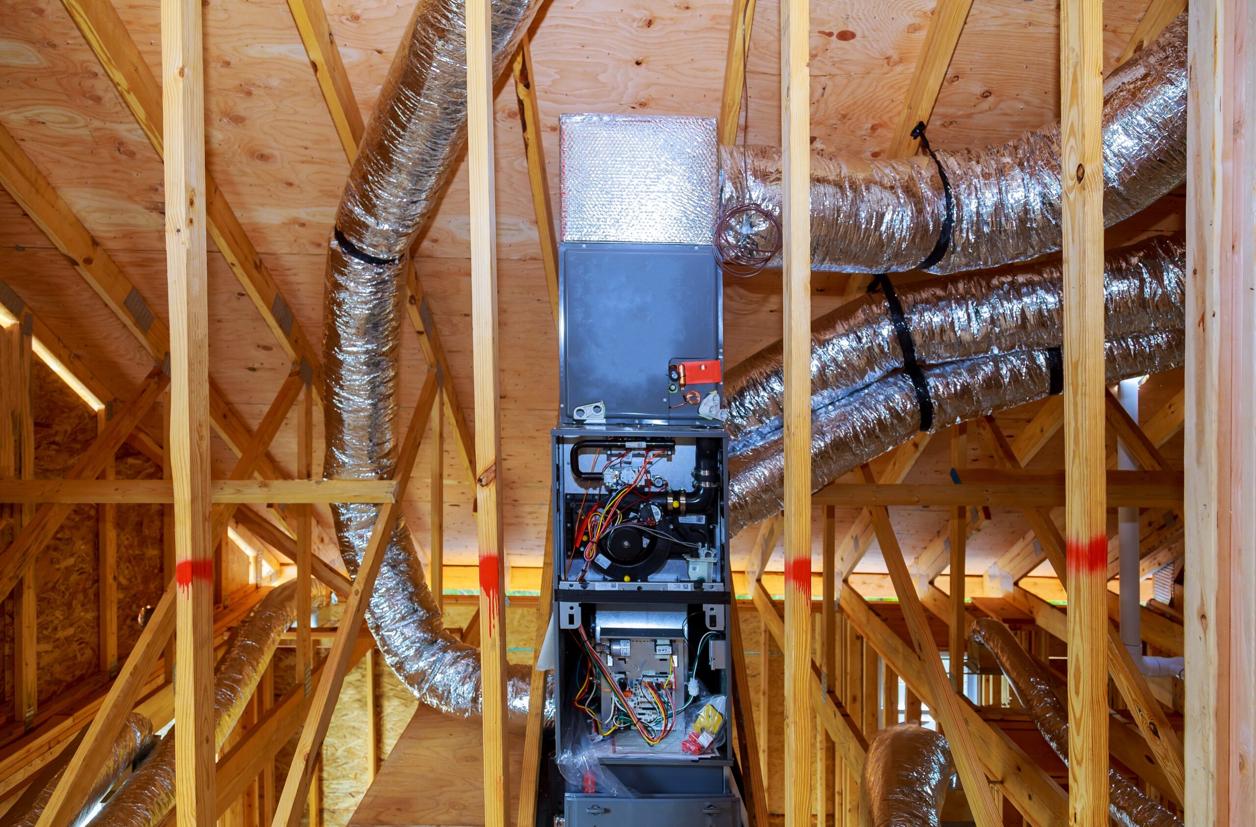 Heating system installation with ductwork in a home construction setting, showcasing metal ducts and HVAC unit among wooden framing.