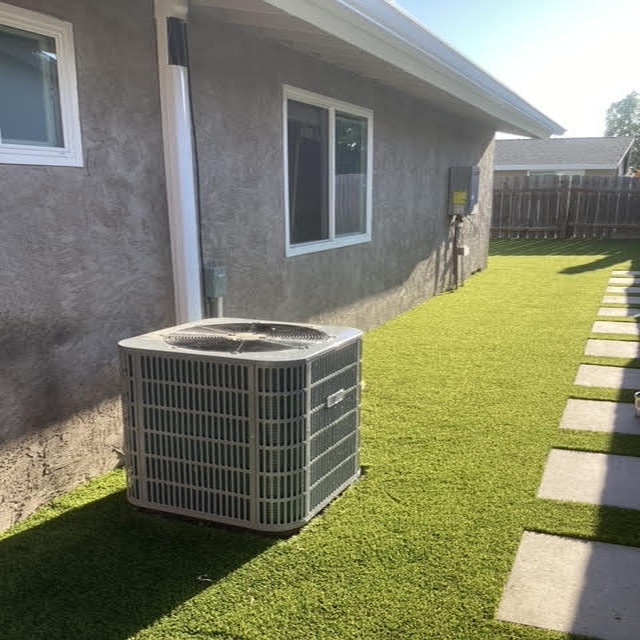 Air conditioning unit installed outside a residential building on artificial grass, highlighting HVAC services offered by Dale-Air in San Diego.