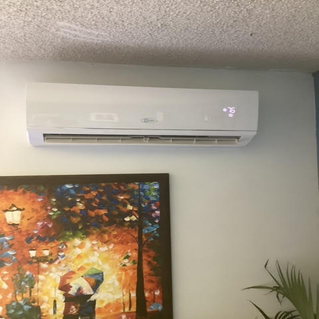 Ductless mini-split air conditioning unit mounted on wall, displaying temperature setting, beside a colorful abstract painting, representing HVAC installation and repair services in San Diego.