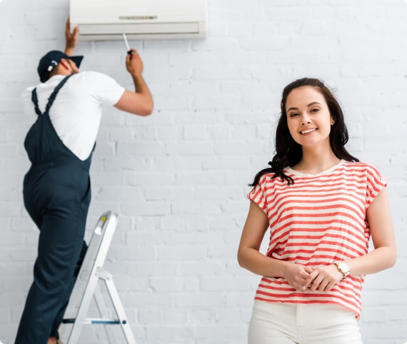 Technician installing air conditioning unit while satisfied customer smiles in foreground, representing quality HVAC services by Dale-Air.