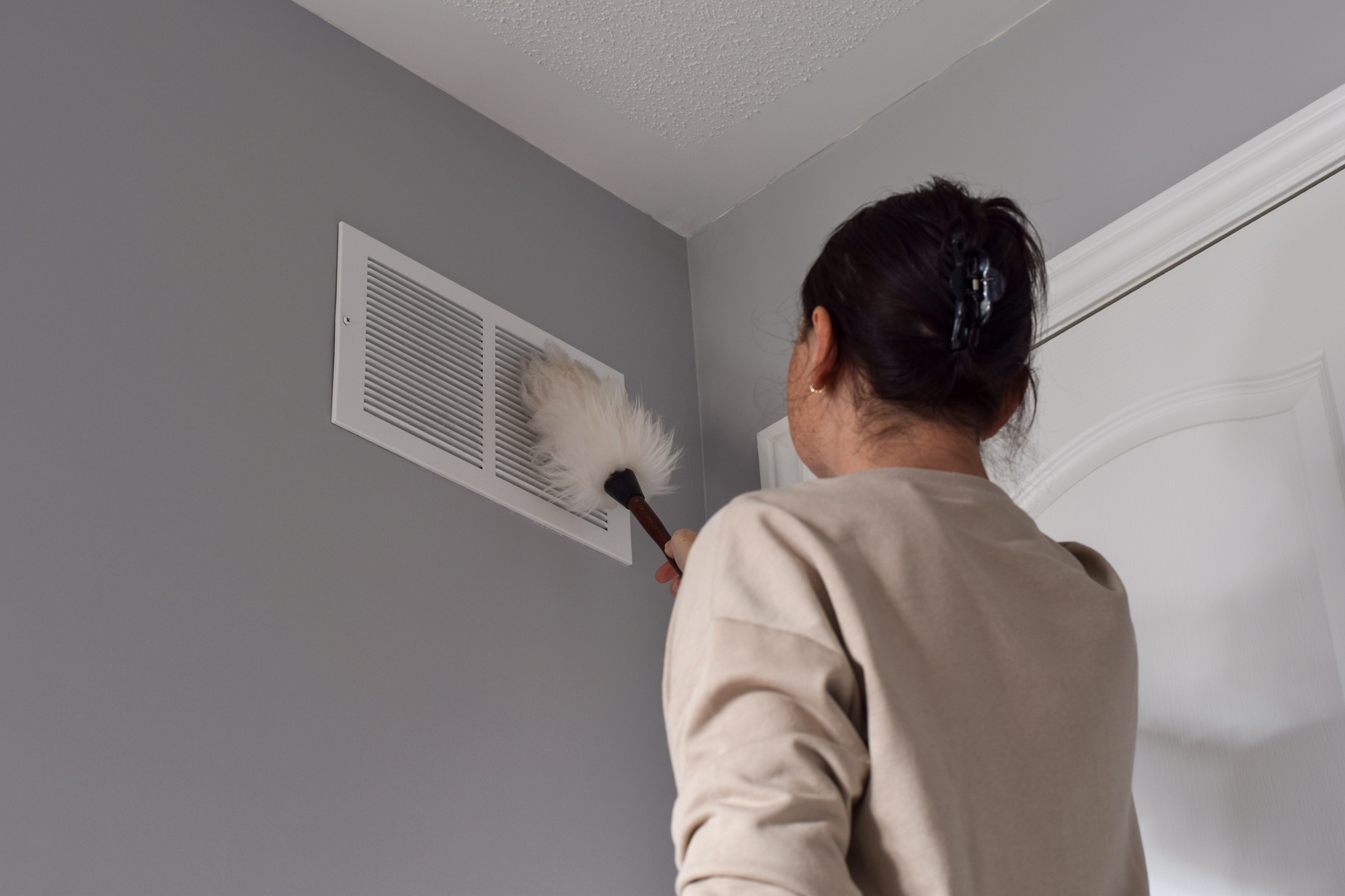 Person cleaning air vent with a duster in a home setting, emphasizing the importance of HVAC maintenance for improved indoor air quality and energy efficiency.