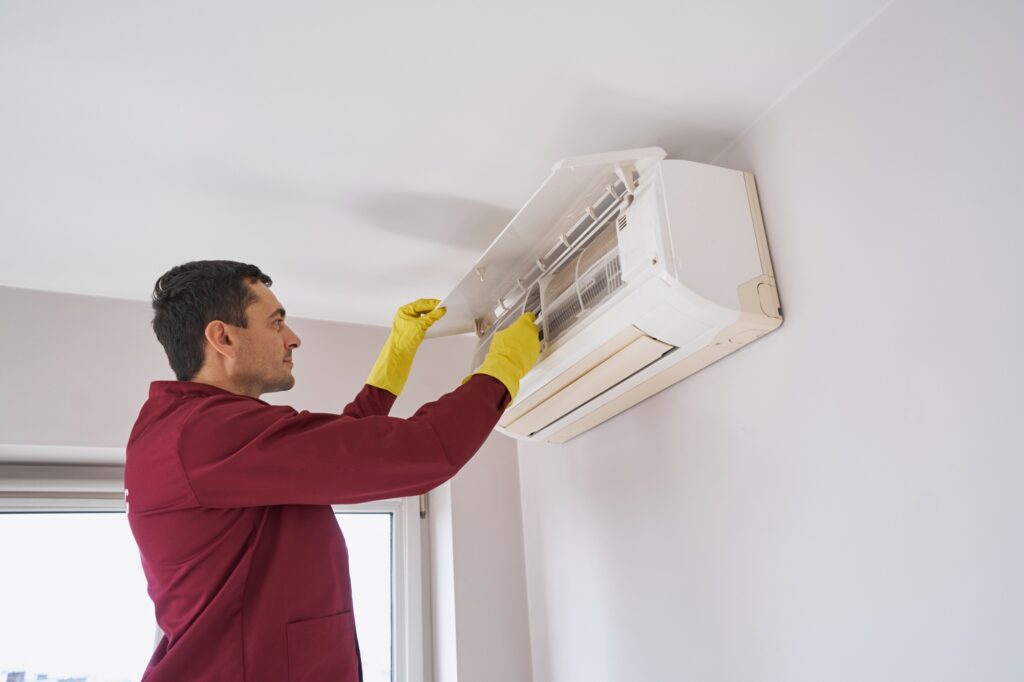 Technician in rubber gloves performing maintenance on a ductless mini-split air conditioning unit, emphasizing HVAC repair services.