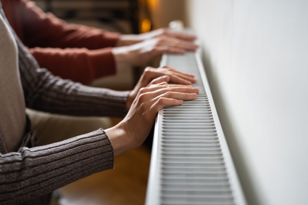 Hands resting on a heating radiator, emphasizing the importance of a functioning heating system for comfort and energy efficiency in homes.