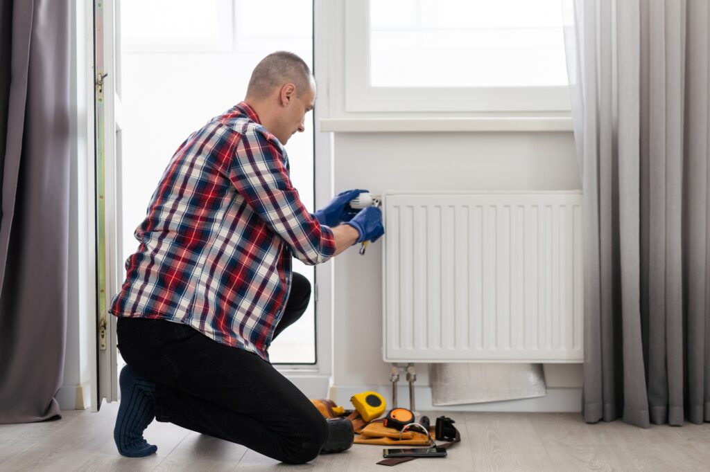 Man repairing a heating radiator with a wrench, surrounded by tools, emphasizing heating repair services for home comfort in San Diego.